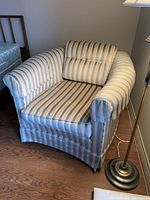 Front view showing the chair's curved arms, striped blue and cream upholstery, and floor skirt covering the base.