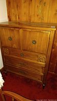 Front view of wooden armoire with two cabinet doors and two drawers, showing decorative metal handles and carved floral details.