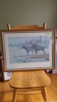 Framed print of moose scene by Brenda Carter on wooden chair showing full framed piece