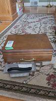 Closed wooden canteen with brass handle on carpet, with table brush and pie lifter in front