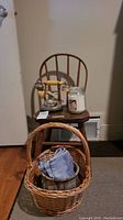 Wooden doll chair with vintage rotary phone and glass candle on seat, wicker basket in front on floor with cloth inside