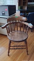 Front angled view of a solid wood spindle back chair on a wood floor indoors.