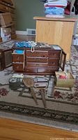 Full view of wooden jewelry box with drawers and side doors open, showing various costume jewelry pieces on top and inside. Multiple decorative trinket boxes arranged in front.