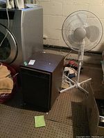 Photo showing Electrohome dehumidifier with paint stains on top and white floor fan behind it, placed on carpet in basement.
