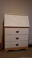 Frontal view of the desk bureau showing the white painted drop top and three white-painted drawers with dark metal handles, natural wood base.