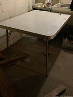 Photo showing the whole rectangular vintage table with patterned white Formica top and chrome framed legs in a basement setting.