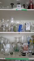 Two shelves densely packed with assorted clear glassware including wine glasses, pitchers, and tumblers.