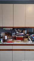 Wide shot of assorted kitchenware items stacked on a kitchen counter, with cabinets above.