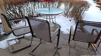 Outdoor patio setup with 3 metal mesh chairs and round glass table with umbrella, view from above showing chair placement and table size