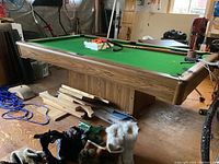 Full view of pool table with balls, cues, triangle rack, and miscellaneous items on floor