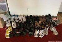 Wide view showing assorted ladies footwear in various styles and colors including sneakers, sandals, slides, and flip-flops arranged on floor.