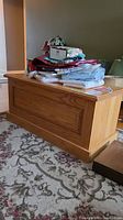 Side front view of oak bench with carved details, showing stacked fabric items on top.