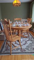 Photo showing full view of the round wooden table with four spindle back chairs arranged around it, part of a living room with a decorative rug underneath.