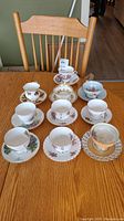 Overview of all 10 teacup and saucer sets arranged on a wooden table with a chair in the background.