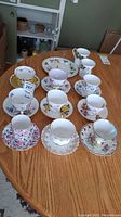 Overall view of all teacups and saucers on wooden table showing variety of floral patterns and gold trim.
