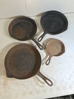 Four vintage cast iron skillets of various sizes placed on white surface, showing overall condition and variation.