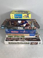 Stack of game boxes including Yahtzee, Clue, Monopoly, Enchanted Forest, Three Little Pigs, Billionaire, and a murder mystery card game.