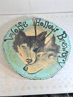 Full view of the painted live edge oak disc sign showing two wolves and brewery name, highlighting cracks and condition.