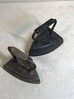 Pair of two vintage cast iron sad irons with triangular bases and black finish, showing minor surface rust and wear.