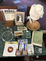 Full overview of assorted vintage and memorabilia items on table including photograph, bonnet, basket, fabric, glass bowls, and paper items