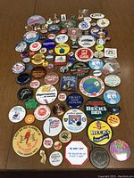 Full collection of vintage pinback buttons and pins arranged on a wooden surface showing various brand logos, political and holiday themes.