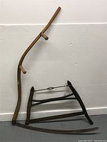 Scythe and harp saw placed against a wall, showing their overall shape and condition.