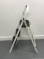 Side view of the slim white metal ladder with three black steps and safety label on side.