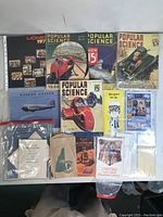 Five Popular Science magazines with vintage automotive and aviation covers along with various vintage paper items on table.