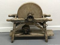 Front view of vintage stone grinding wheel mounted on a wooden frame with motor underneath. Shows full apparatus including wheel, frame, and motor.