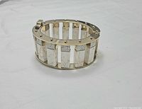 Wide gold-tone bracelet with gold studs, featuring rectangular white marbled stones and small clear rhinestone bands, shown from top angle.
