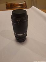 Canon EF 75-300mm telephoto zoom lens standing upright on white surface in indoor setting, showing full lens barrel with zoom scale and USM branding.