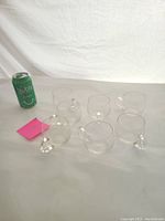 Photo of seven small clear glasses, each with a handle, arranged on a surface with a soda can for scale.