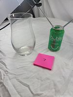 Clear glass vase with a curved body and thick base next to a green sparkling water can for size reference.