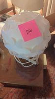 Photo of white Ikea table lamp with flower petal design lampshade and white wire base from above, placed on wooden table.