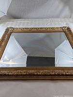 Front view of rectangular wall mirror showing decorative gold frame and beveled glass reflecting photo lighting setup and gray backdrop.