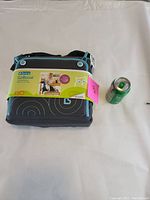 Photo of Brica GoBoost travel booster seat in dark blue and light blue color with soft carrying case and standard soda can for size comparison.