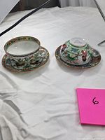 Two vintage Chinese tea cups on a white cloth; one cup is upright and the other is upside down showing the underside with markings.