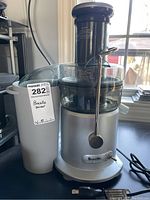 Full view of Breville Juice Fountain juicer showing silver base, clear plastic top, and locking arm, with power cord.