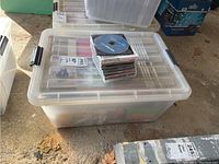 Large plastic bin with many CDs stored inside, and a few stacked on top of the closed lid.