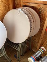 Five round plastic low-top event tables stacked against a wall showing smooth tabletop surfaces and some dirt marks.