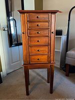 Front view of the wood jewelry cabinet showing five drawers and side doors, standing on four legs.