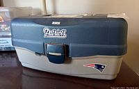 Full view of New England Patriots tinted blue and gray plastic tackle box with logo on front and locking clasp.