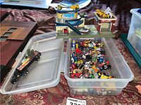 Top-down view of micro vehicles including cars and trucks inside a plastic storage container along with a police station playset on top of the container.