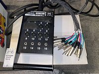 Overview of the black Hosa Pro-Conex stage box with 12 labeled XLR microphone inputs and additional 1/4" jacks, showing taped off connections.