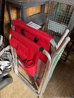 Folded red fabric lounge chair showing side pockets and metal frame, stacked with two other chairs