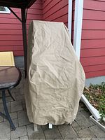 Beige protective cover placed over stacked patio chairs on a brick patio with red siding background