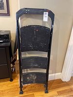 Front view of black metal step ladder showing three wide steps with paint splatters and rubber feet