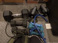 Overhead view of assorted dumbbells in different weights including hex and vinyl-coated, resistance strap and handle grips visible on puzzle mat surface.