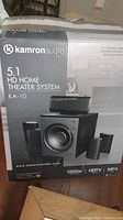 Box showing Kamron Audio branding with image of 5.1 HD home theater system including subwoofer and five speakers, model KA-10, 1500 watt