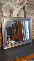 Front view of beveled edge mirror showing textured frame and reflections of furniture and lighting.